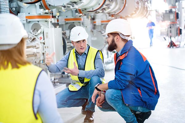 Ausbilder sitzt mit Studierenden in der Hocke und erklärt eine Maschine