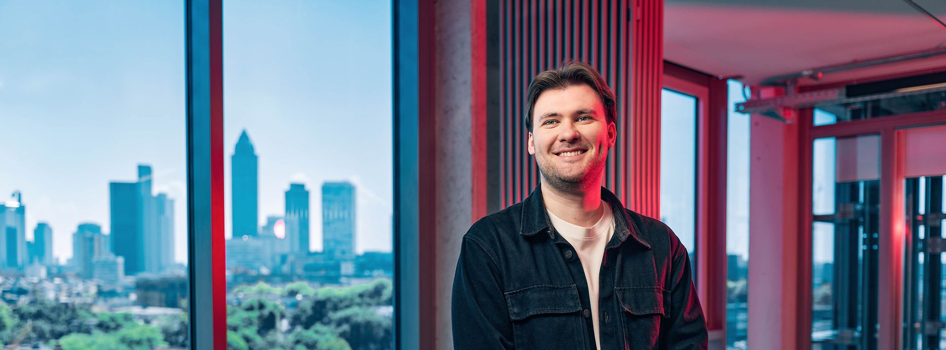 Junger man lächelt vor Fenstern in die Kamera
