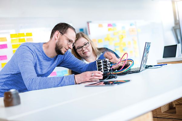 © Mainova/AndreFormer Ausbilder erklärt Auszubildende ein elektronisches Gerät was auf dem Tisch liegt