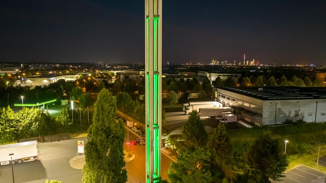 Grün-leuchtende Säule im Dunkeln mit der Frankfurter Skyline im Hintergrund