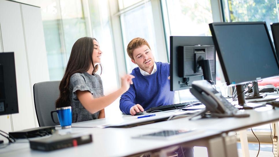 Zwei Studierende sitzen am Monitor und besprechen den Sachverhalt am Monitor