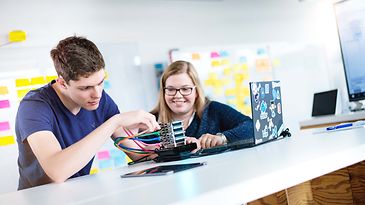 © Mainova/AndreFormer Zwei Auszubildende sitzen am Tisch und stecken Kabel in ein Elektronik Bauteil