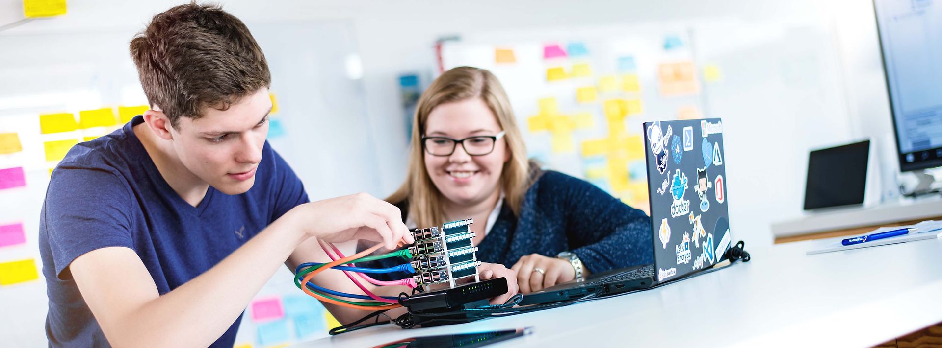 © Mainova/AndreFormer Zwei Auszubildende sitzen am Tisch und stecken Kabel in ein Elektronik Bauteil