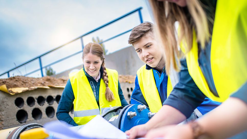 Gruppe Studenten sitzen auf einer Baustelle und betrachten einen Bauplan